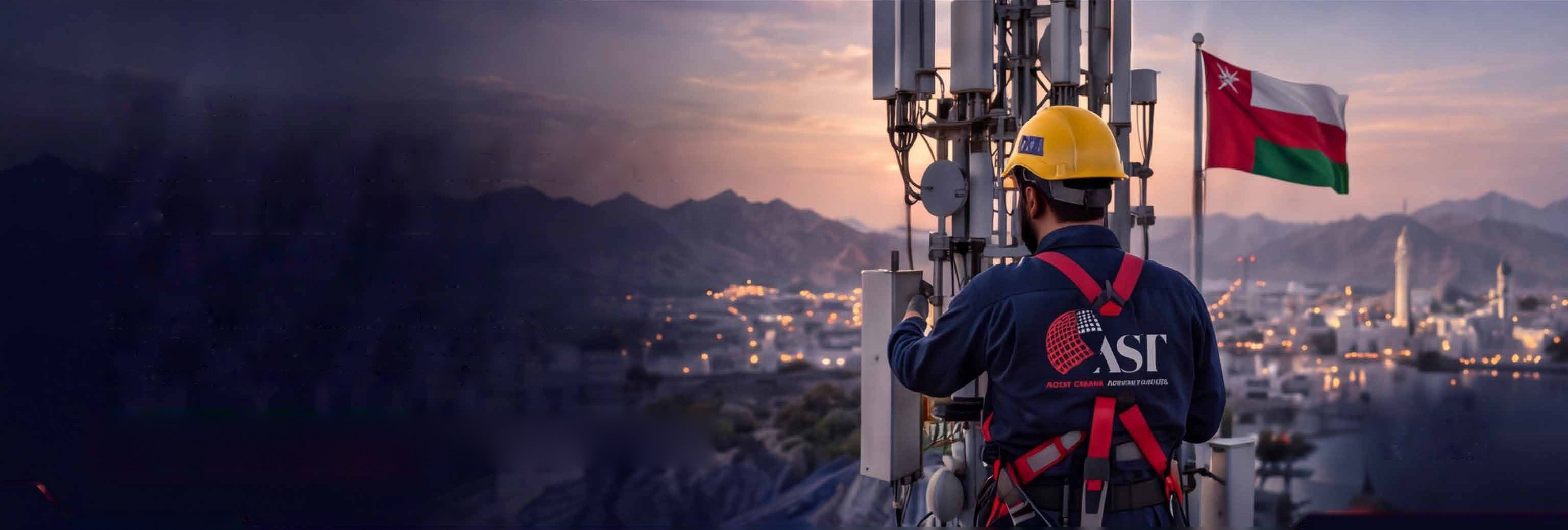 AST technician servicing a telecom mast above Muscat, with the flag of Oman